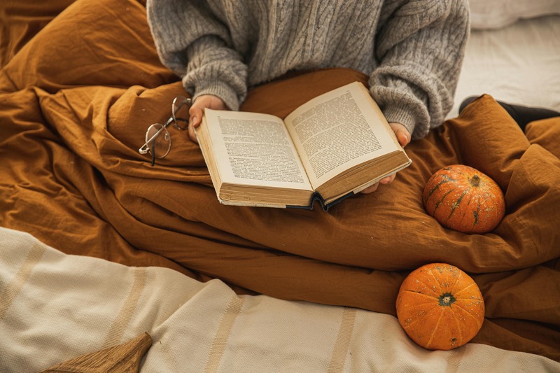 Person relaxing with a book under a soft blanket in the evening