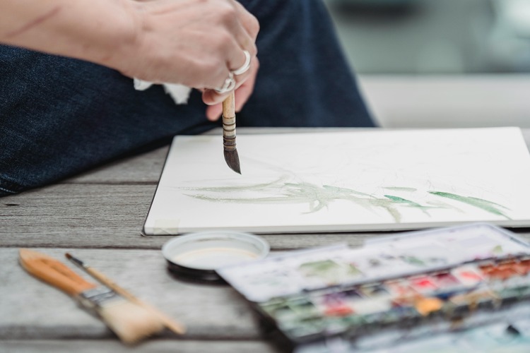 Woman painting with watercolours at a sunlit table as a creative hobby